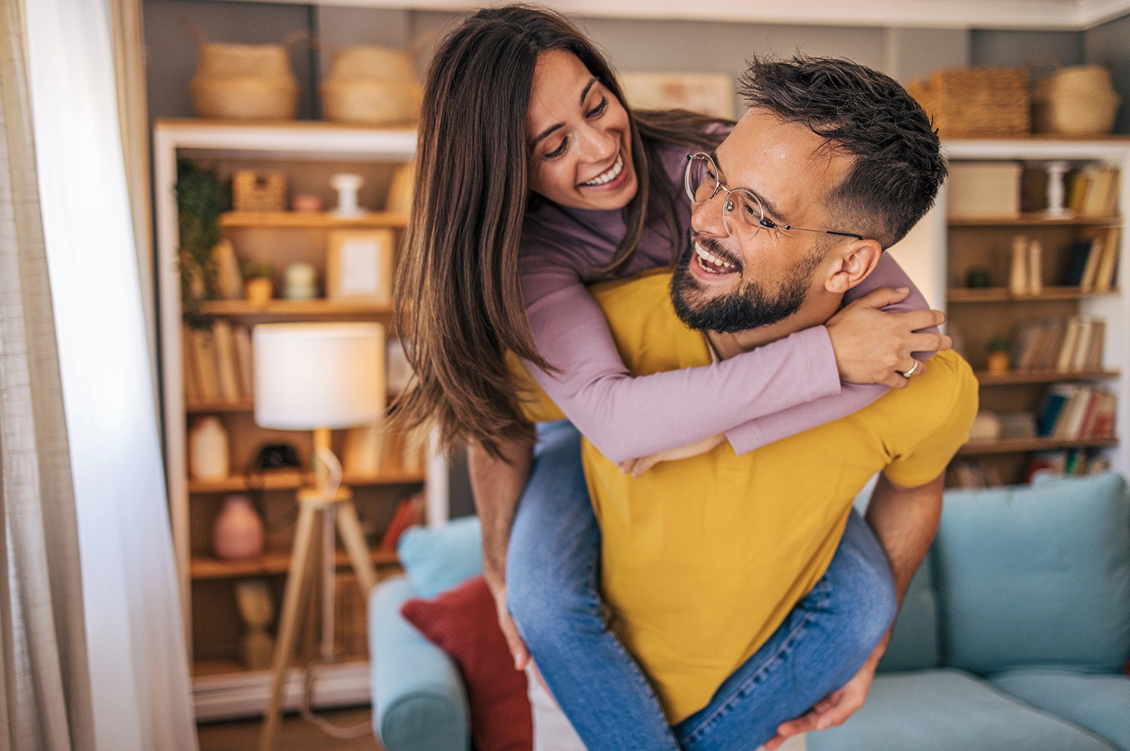 A woman jumps on a man's back playfully as they both smile at each other. 