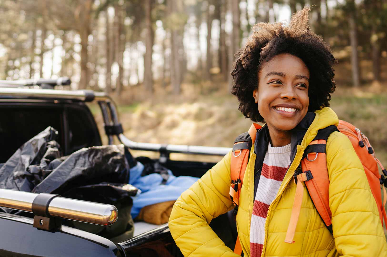 A young women smiles and leans on the bed of her pickup truck parked in the woods. A young women smiles and leans on the bed of her pickup truck parked in the woods.