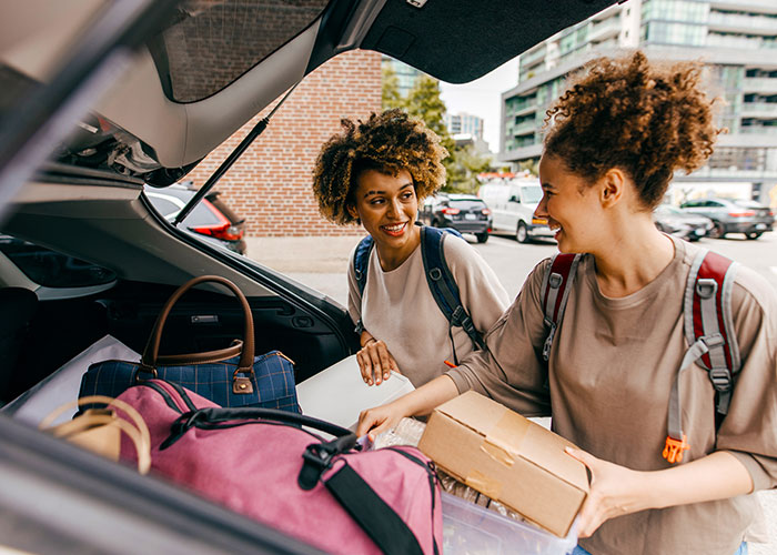 Two college students unload their possessions from the back of a car.